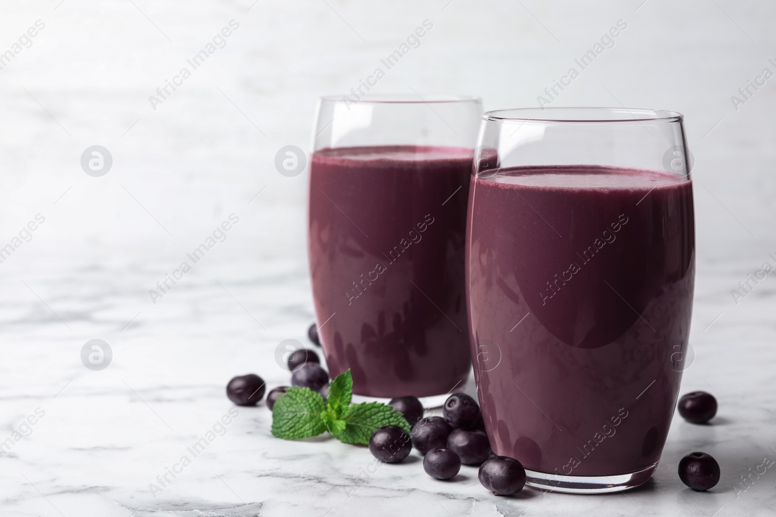 Photo of Tasty acai drink in glasses and berries on marble table