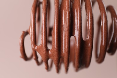 Whisk with chocolate cream on light background, closeup