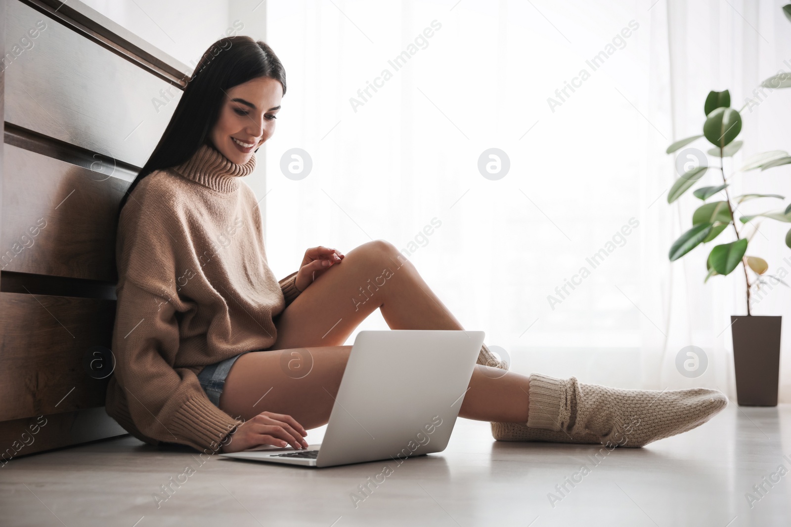 Photo of Woman with laptop sitting on warm floor at home. Heating system