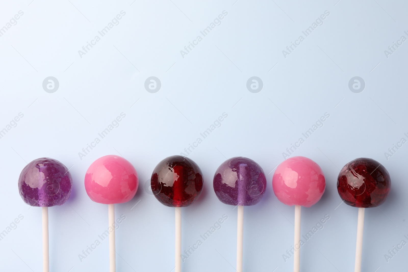 Photo of Tasty lollipops on light blue background, flat lay. Space for text