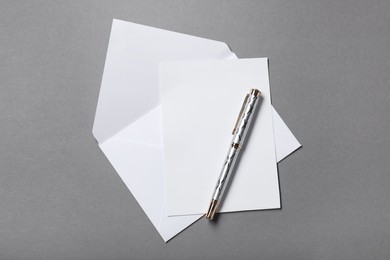 Blank sheet of paper, letter envelope and pen on grey background, top view