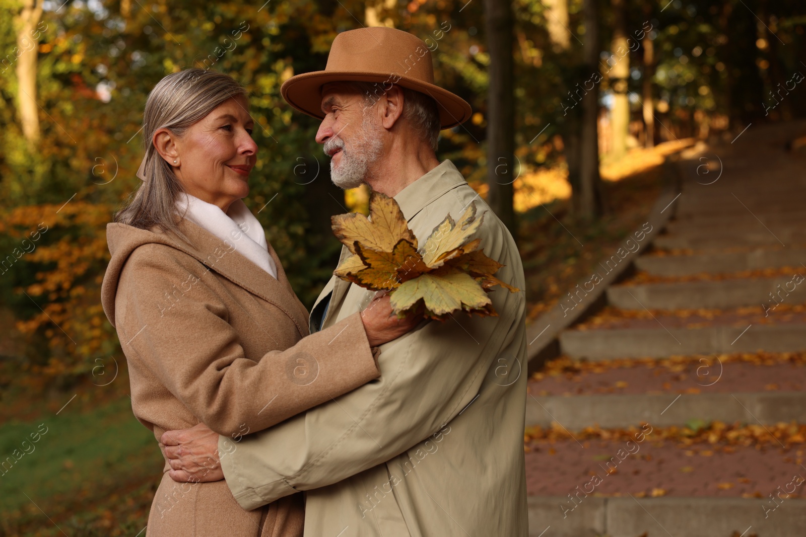 Photo of Affectionate senior couple with dry leaves in autumn park, space for text