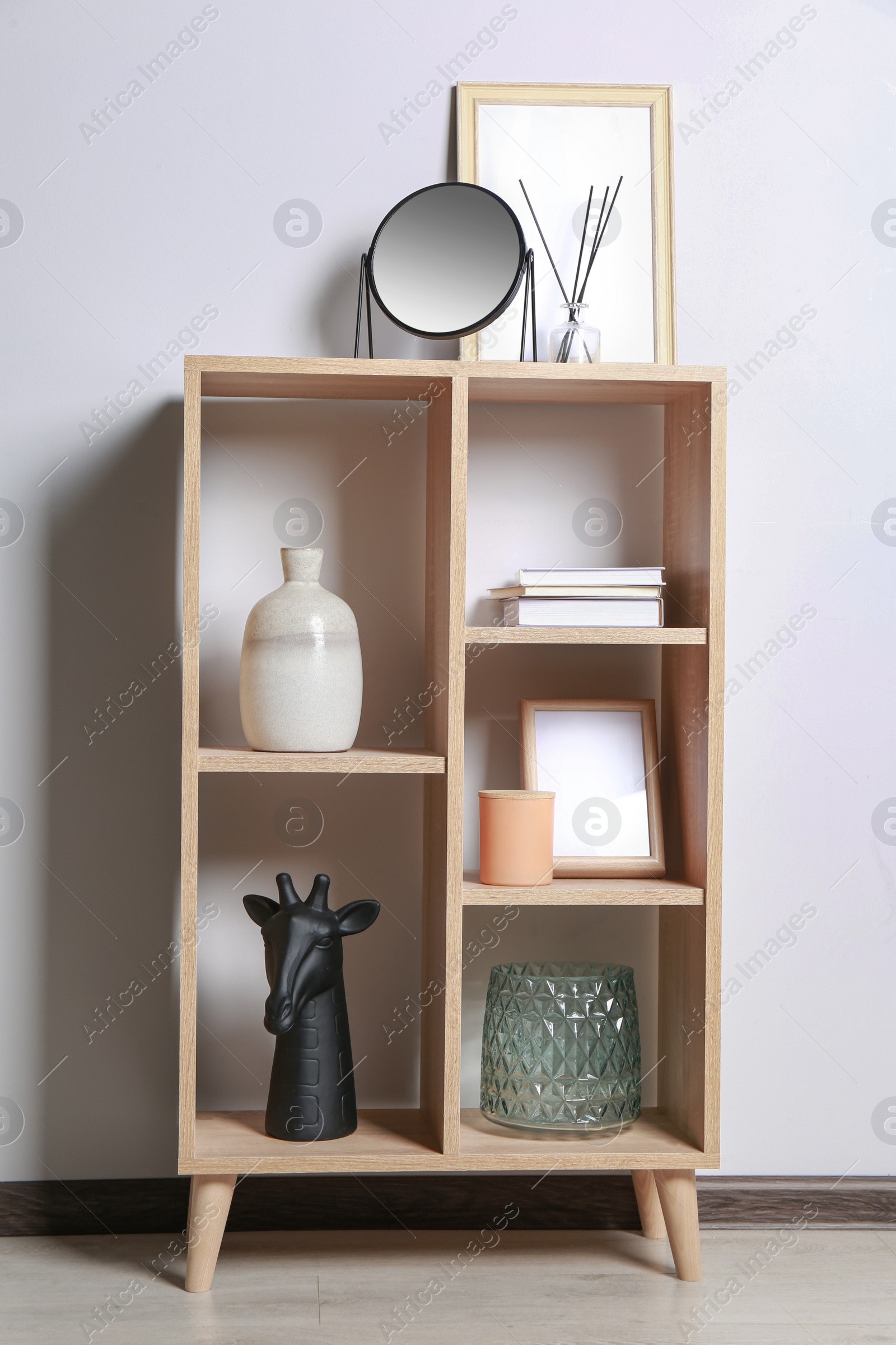 Photo of Stylish mirror, reed diffuser and picture frame on shelf near light wall. Interior design