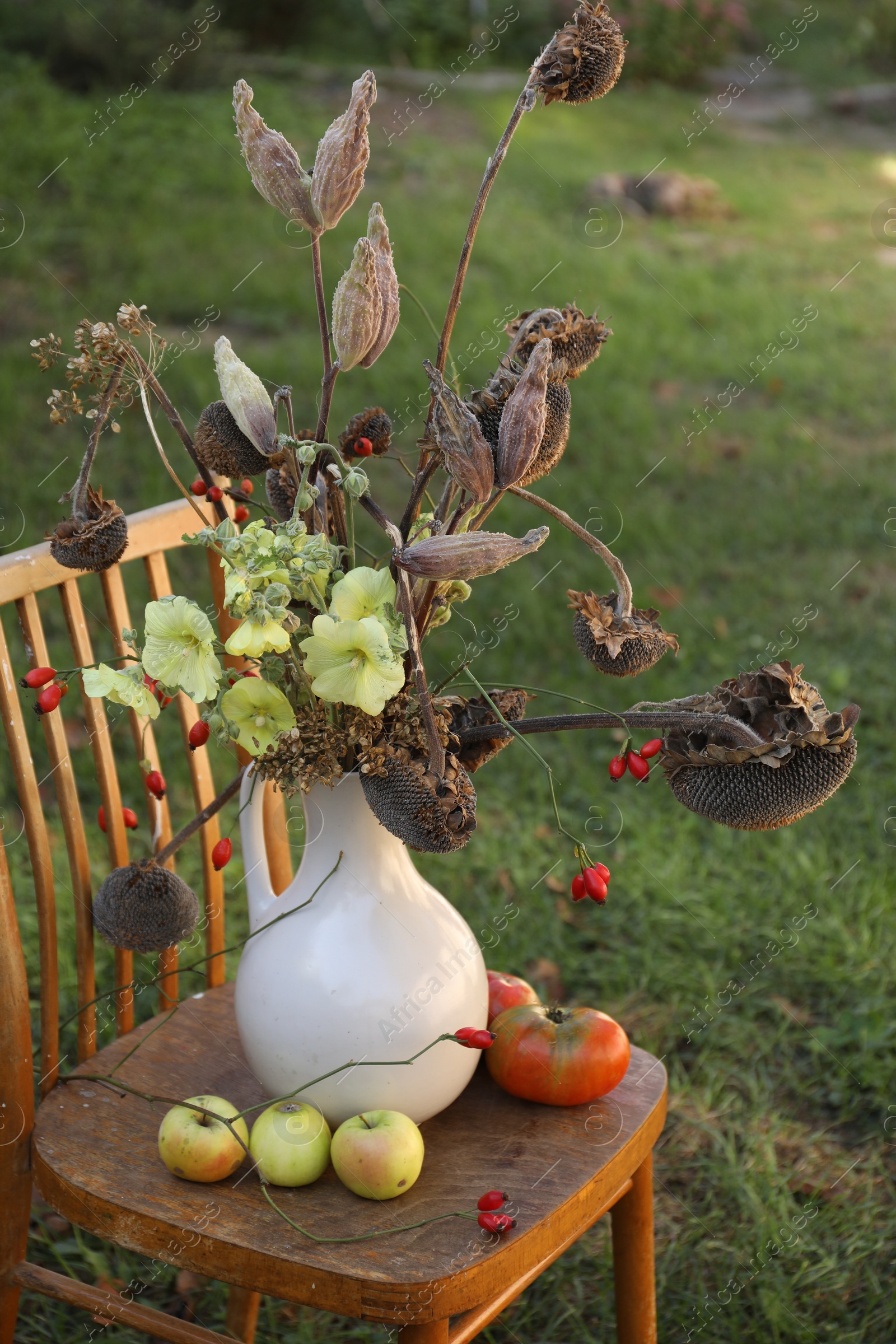 Photo of Composition with beautiful flowers, dry sunflowers and apples on wooden chair outdoors. Autumn atmosphere