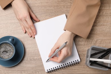 Photo of Woman writing in notebook at wooden table, top view