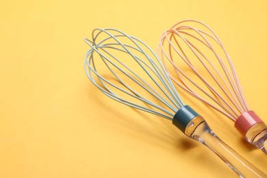 Two whisks on yellow background, closeup. Space for text