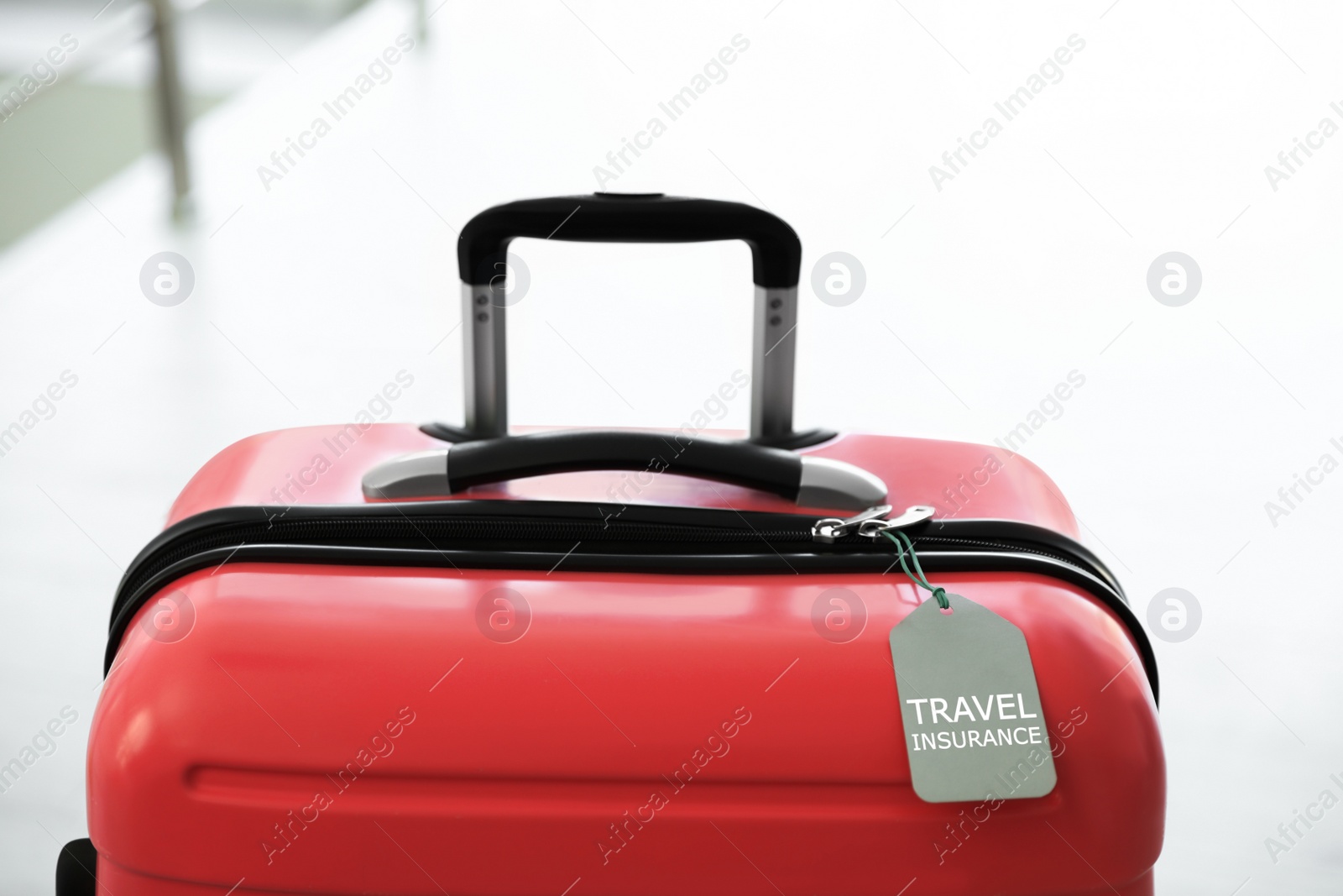 Photo of Stylish suitcase with travel insurance label on blurred background, closeup. Space for text