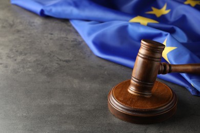 Photo of Wooden judge's gavel and flag of European Union on grey table. Space for text