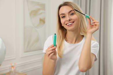 Beautiful happy woman applying mascara at home, space for text