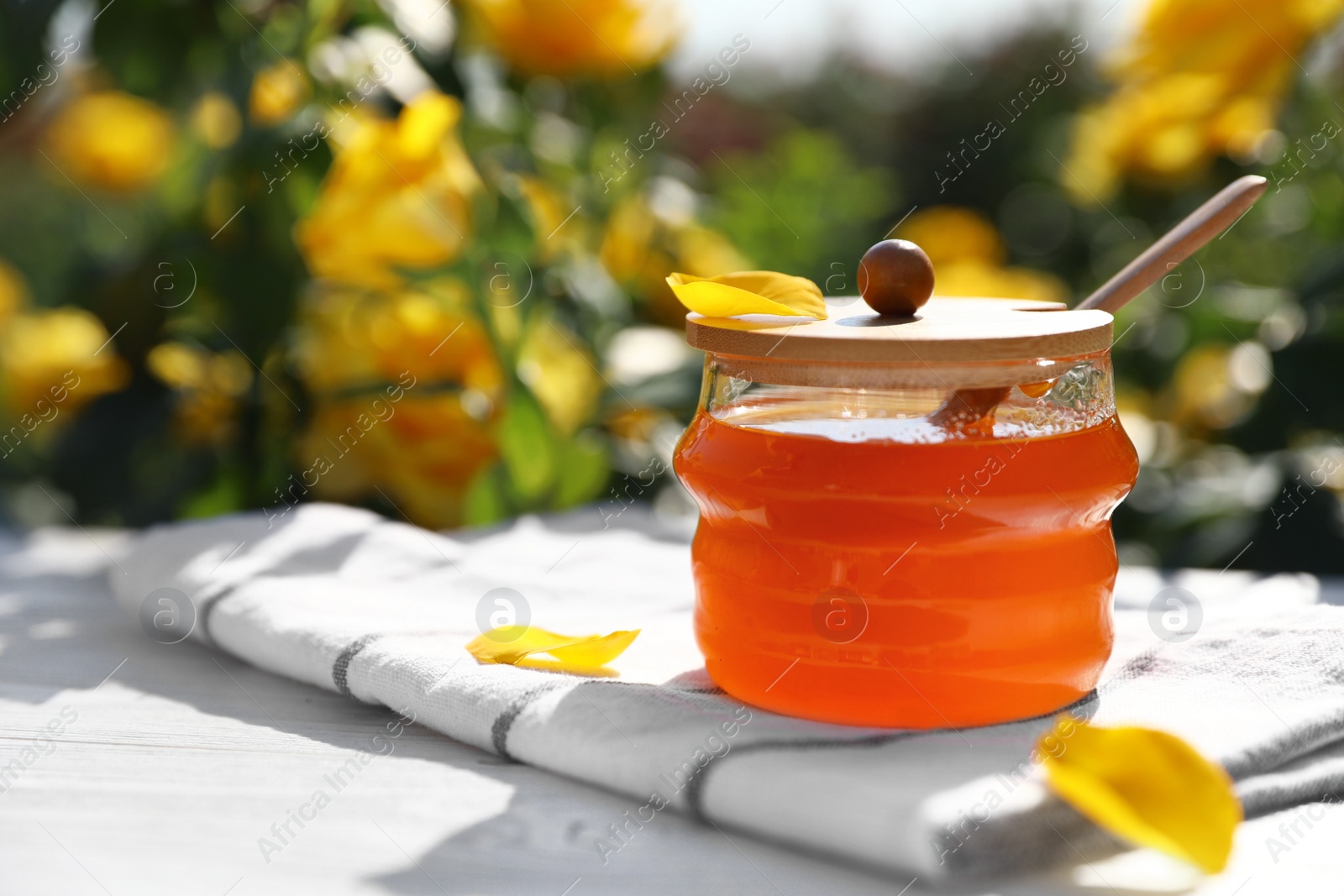 Photo of Jar with fresh rose honey on white wooden table outdoors. Space for text