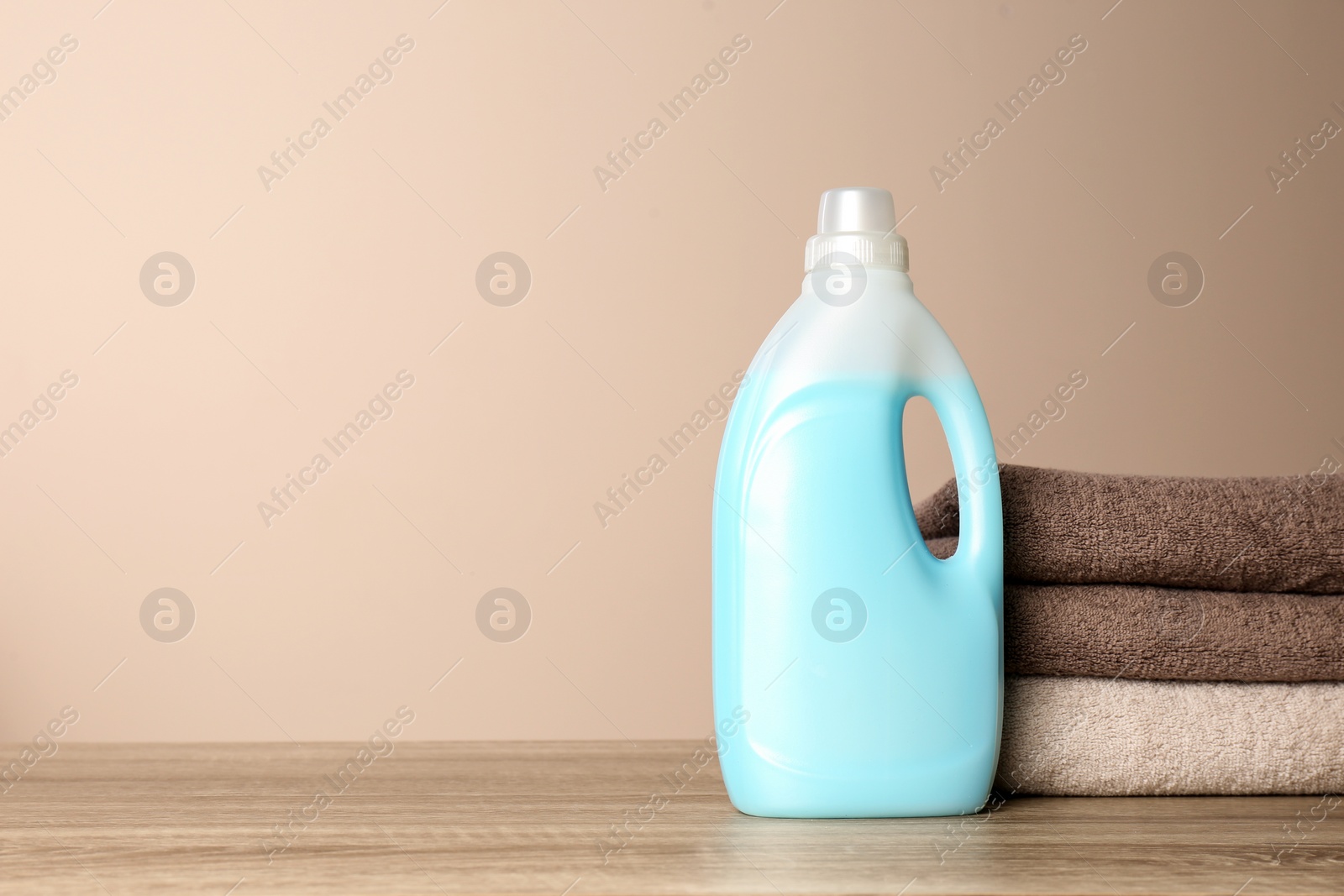 Photo of Bottle of detergent and clean towels on table against color background, space for text. Laundry day