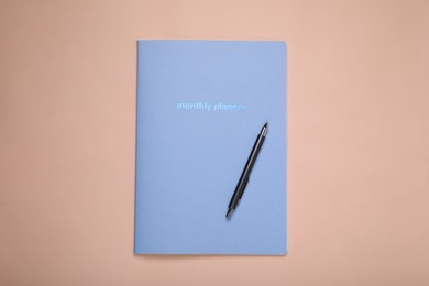 Photo of Monthly planner and pen on beige background, top view