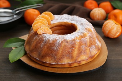 Homemade yogurt cake with tangerines, powdered sugar and green leaves on wooden table