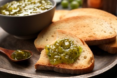 Photo of Toasts with delicious gooseberry jam on wooden plate, closeup