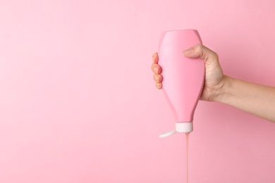 Photo of Woman pouring cosmetic product from bottle on color background, closeup. Space for text