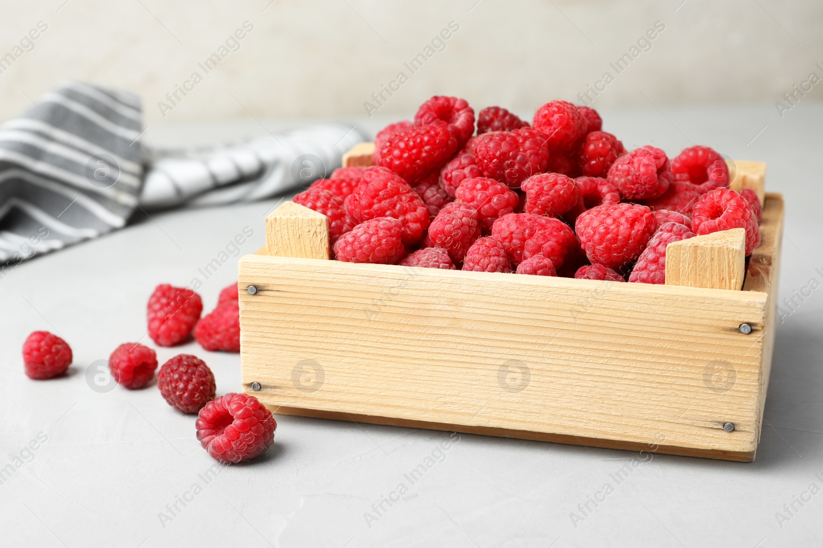 Photo of Wooden crate with delicious ripe raspberries on table against light background