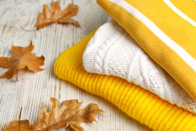 Photo of Stack of folded knitted sweaters and autumn leaves on table. Space for text