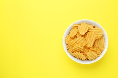 Photo of Bowl of tasty ridged potato chips on yellow background, top view. Space for text
