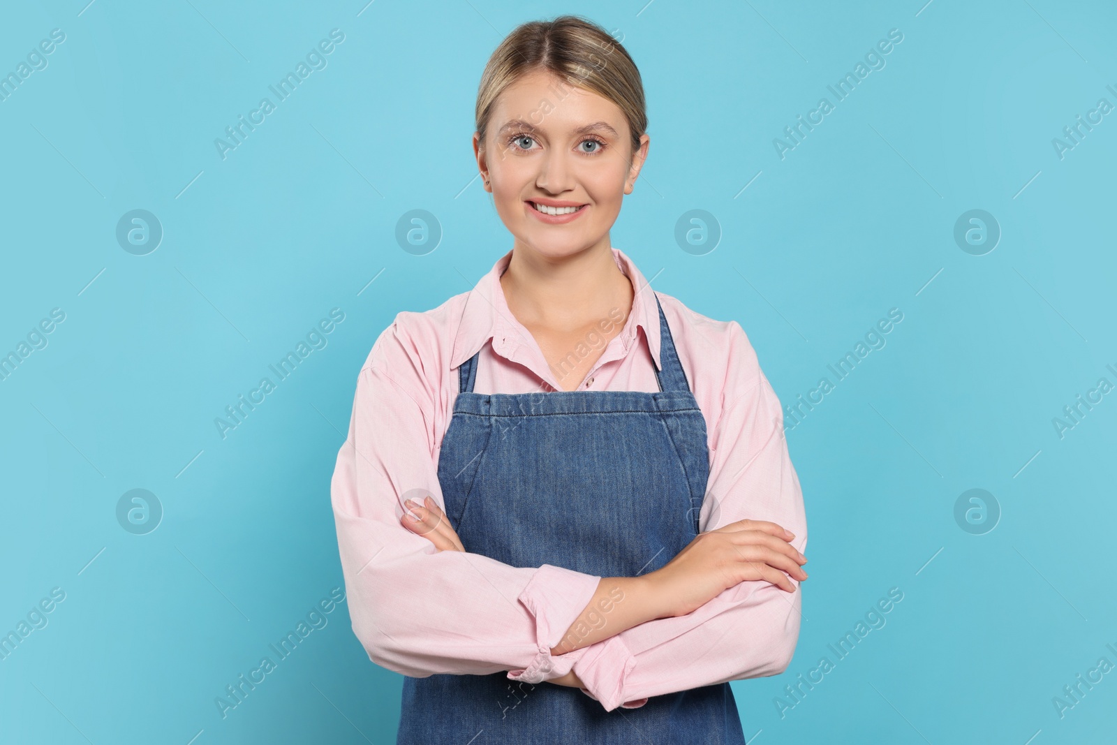 Photo of Beautiful young woman in denim apron on light blue background