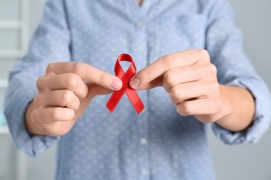 Woman holding red awareness ribbon indoors, closeup. World AIDS disease day