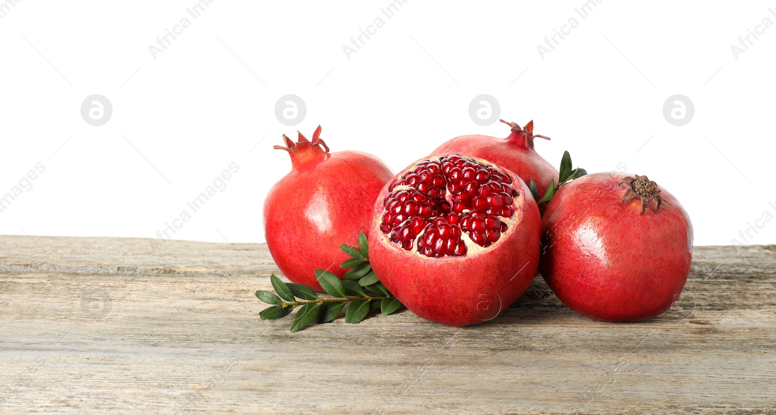 Photo of Fresh pomegranates and green leaves on wooden table against white background, space for text