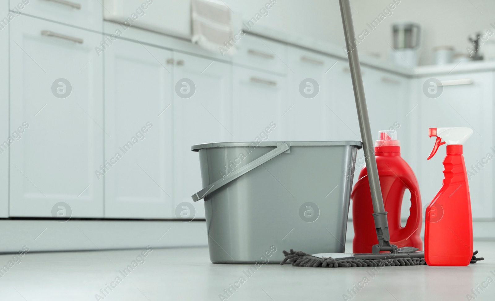 Photo of Mop, detergents and plastic bucket in kitchen, space for text. Cleaning supplies