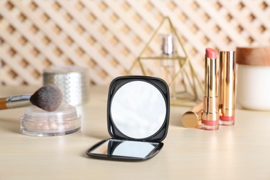 Photo of Stylish pocket mirror and cosmetic products on beige table