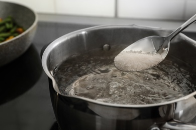 Salting boiling water in pot on stove, closeup