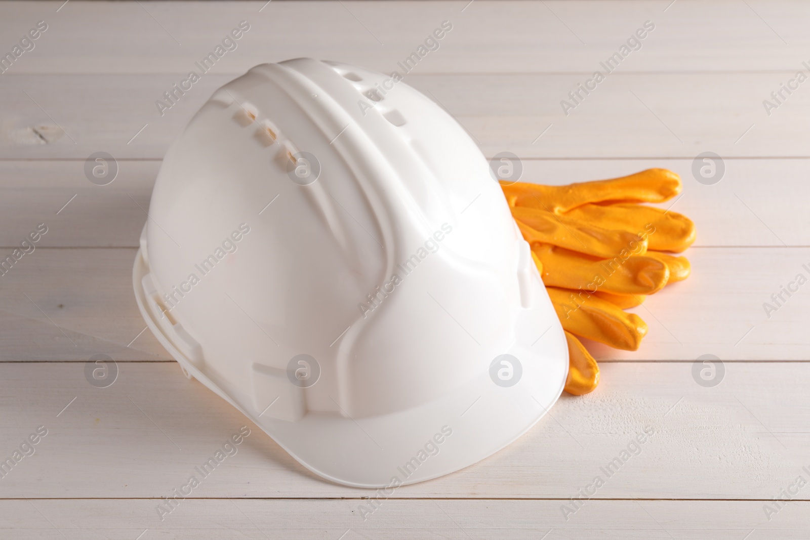 Photo of Hard hat and gloves on white wooden table. Safety equipment