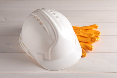 Photo of Hard hat and gloves on white wooden table. Safety equipment