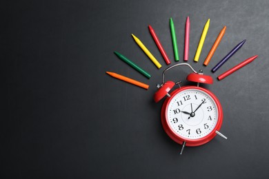 Photo of Alarm clock and colorful pencils on blackboard, flat lay with space for text. School time