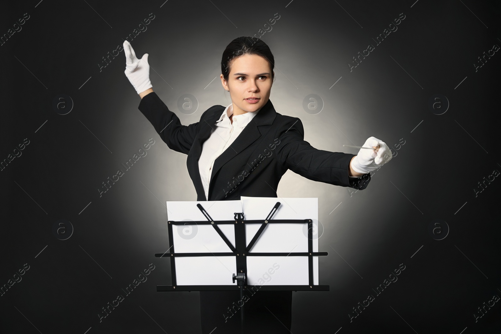 Photo of Professional conductor with baton and note stand on black background