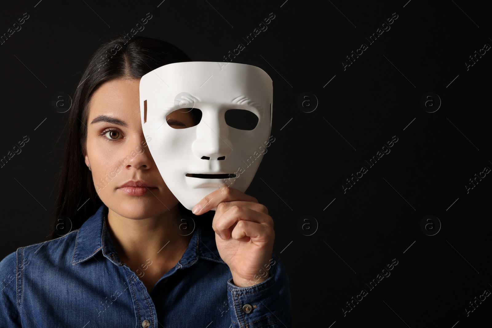 Photo of Multiple personality concept. Woman with mask on black background, space for text