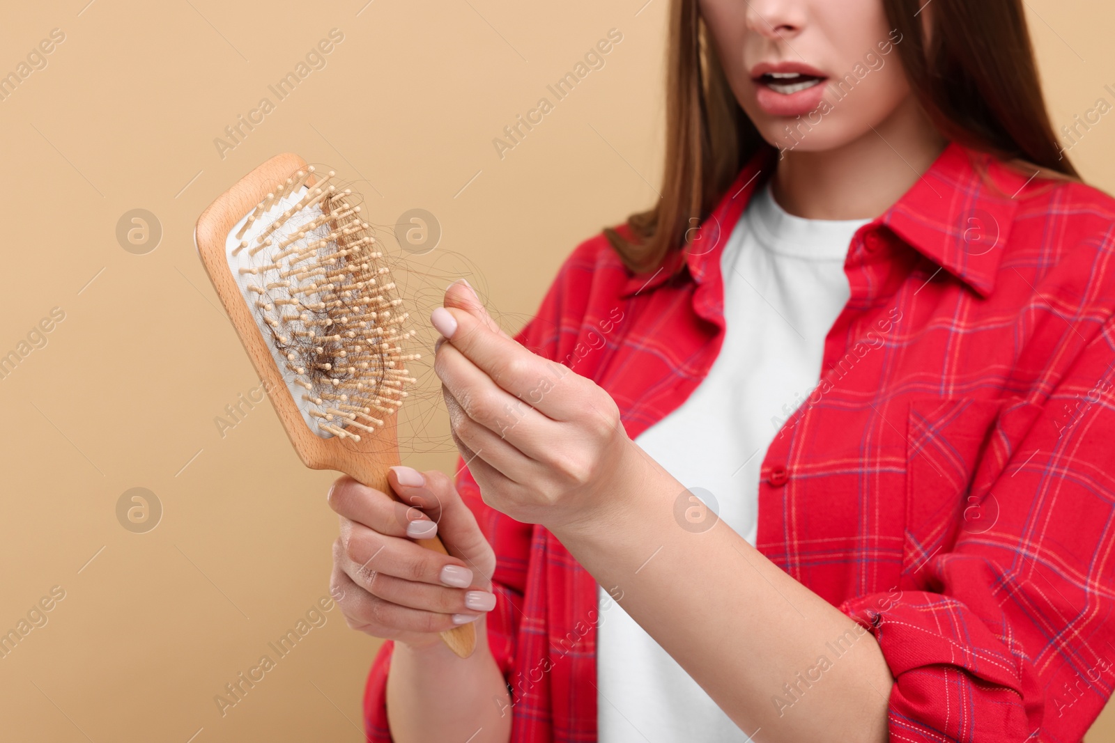 Photo of Woman untangling her lost hair from brush on beige background, closeup. Alopecia problem