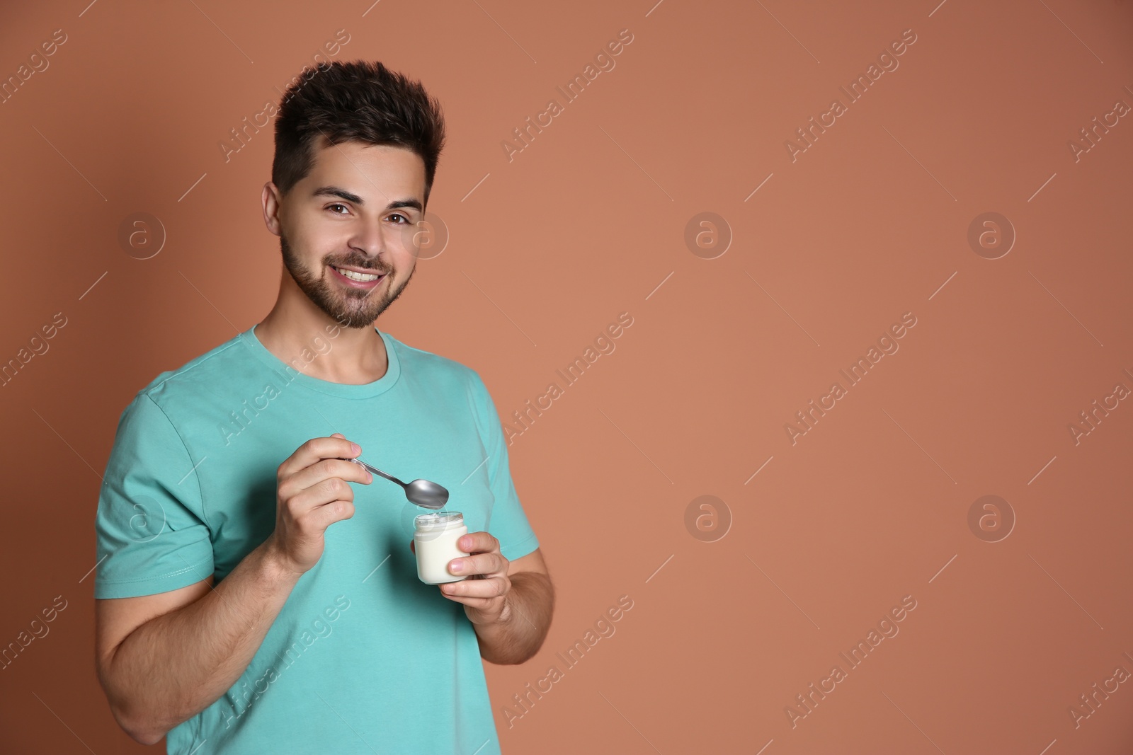 Photo of Happy young man with yogurt and spoon on brown background. Space for text