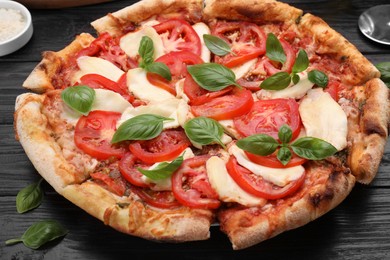 Photo of Delicious Caprese pizza on black wooden table, closeup