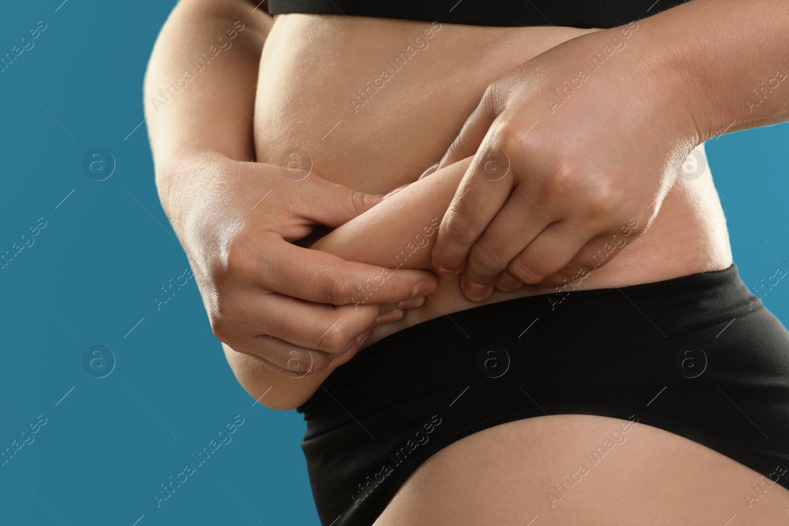 Photo of Woman touching belly fat on light blue background, closeup. Overweight problem