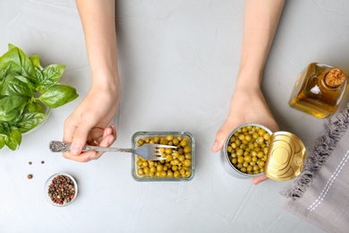 Woman with canned green peas at table, top view