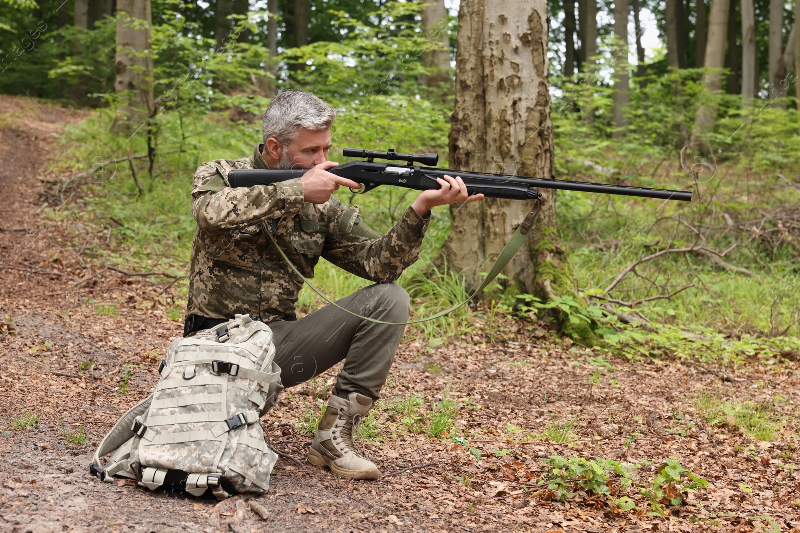 Photo of Man wearing camouflage and aiming with hunting rifle in forest