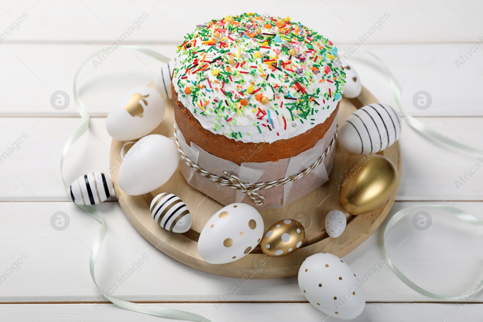 Photo of Traditional Easter cake with sprinkles and painted eggs on white wooden table