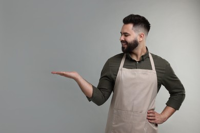 Photo of Smiling man in kitchen apron holding something on grey background. Mockup for design