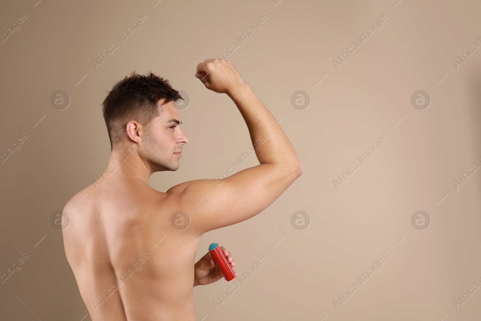 Photo of Young man applying  deodorant to armpit on beige background. Space for text
