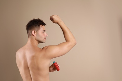 Young man applying  deodorant to armpit on beige background. Space for text