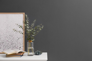 Beautiful eucalyptus branches on white table near black wall in modern room, space for text. Interior design