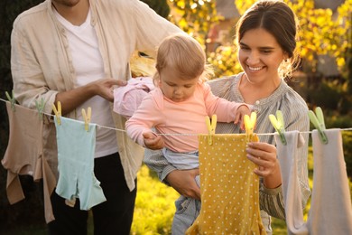 Happy family hanging baby clothes with clothespins on washing line for drying in backyard