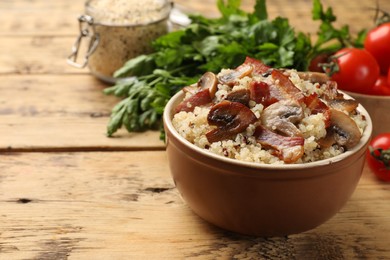 Photo of Tasty quinoa porridge with fried bacon and mushrooms in bowl on wooden table, closeup. Space for text