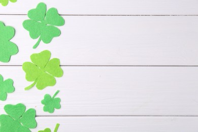 Photo of St. Patrick's day. Decorative green clover leaves on white wooden table, flat lay. Space for text