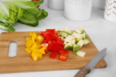 Wooden board with cut vegetables and knife on kitchen table