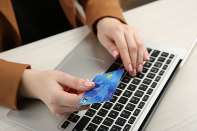 Photo of Online payment. Woman with credit card using laptop at white table, closeup