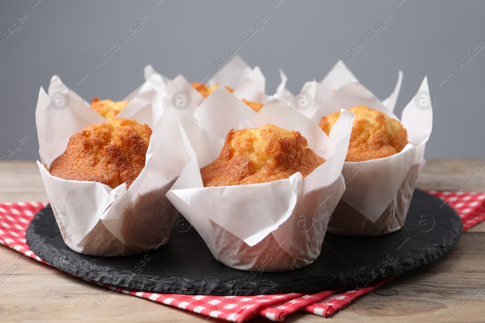 Photo of Delicious sweet muffins on wooden table against grey background, closeup